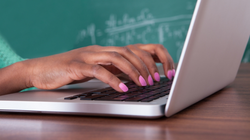 A person with pink nails types on a laptop, ready to launch a quiz with participants in a classroom
