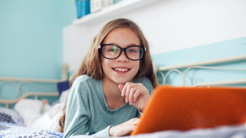 A young girl with glasses smiles while using a laptop