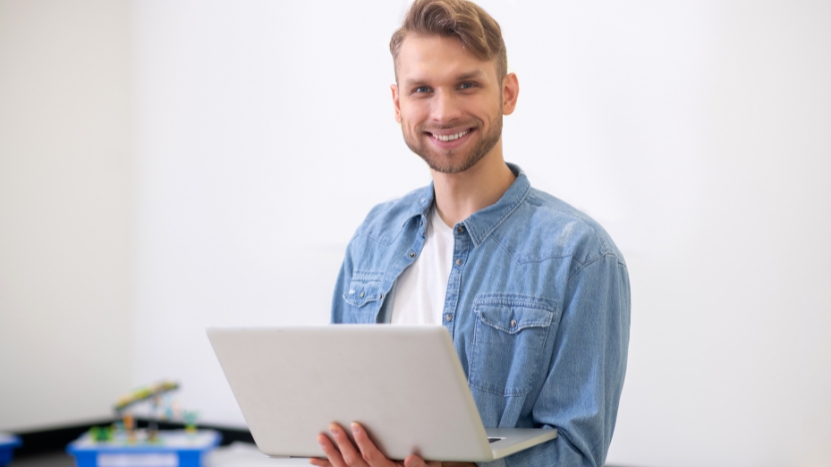 A teacher holds a laptop and smiles, showing how data and reporting automation supports teacher productivity