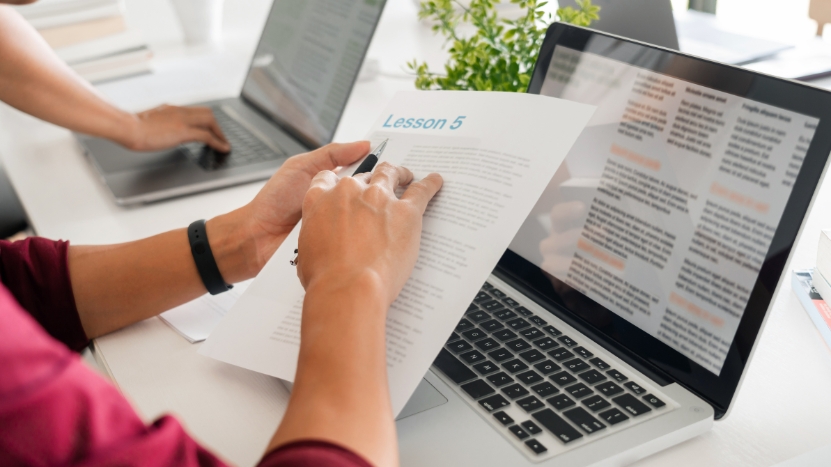 A student reviews printed notes alongside digital text on a laptop to track and correct mistakes