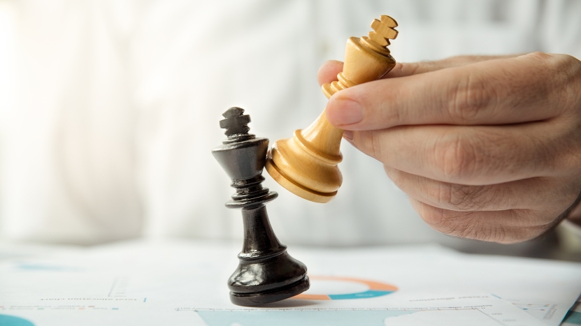 A hand moves a gold chess king toward a black king over financial charts on a desk