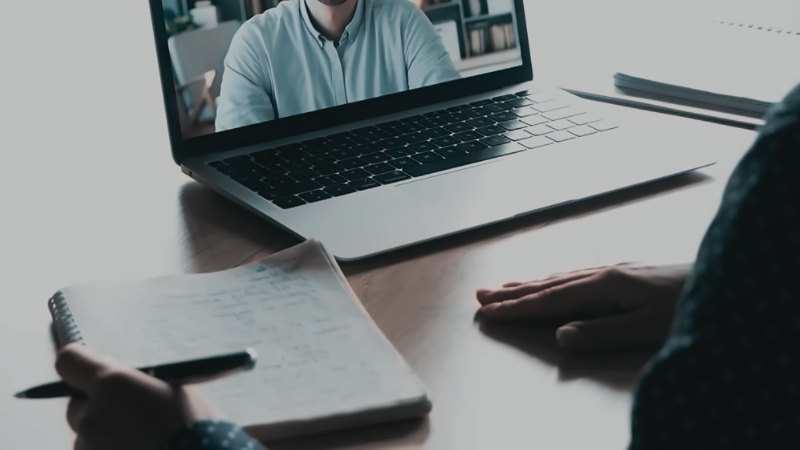 A Person Is Taking Notes While Attending an Online Class on Their Laptop