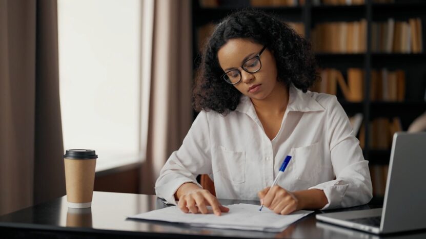 A woman reviews paperwork at a desk in a library setting