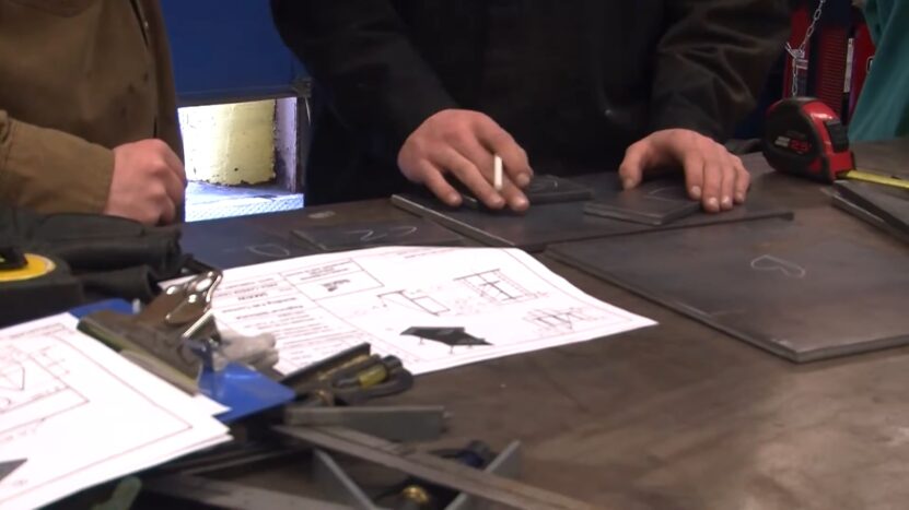 Close-up of hands working with metal pieces and welding blueprints on a table in a workshop