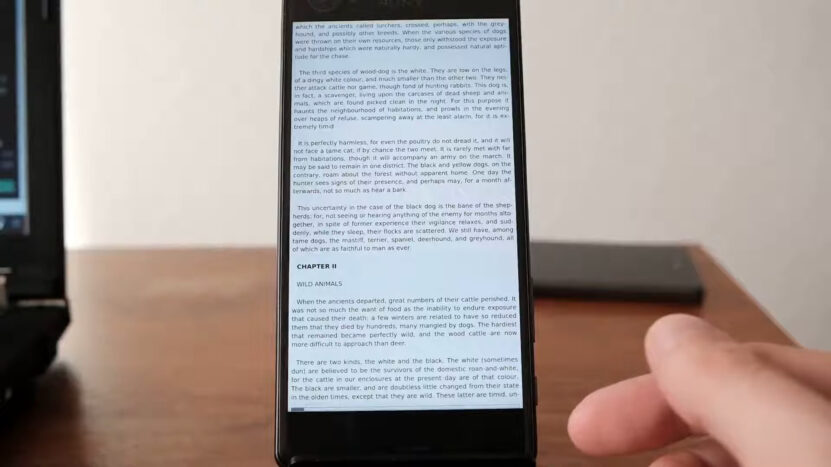 Close-up of a smartphone screen displaying an eBook with a hand scrolling on FBReader app