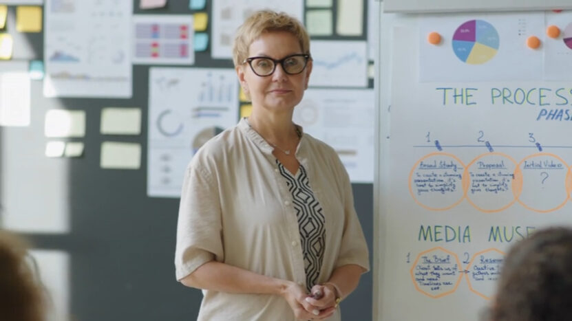 A woman stands confidently in front of a whiteboard filled with charts and diagrams