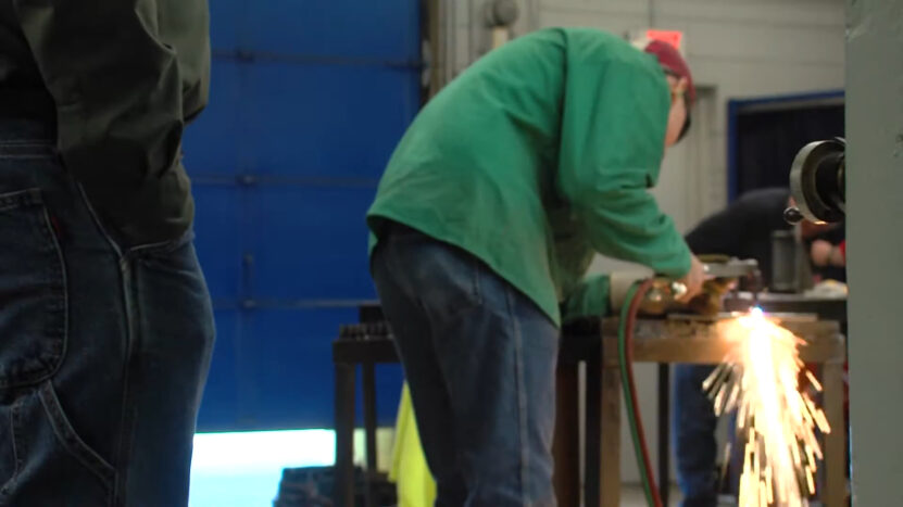 Person in a green welding jacket working with equipment, creating sparks in an industrial workshop