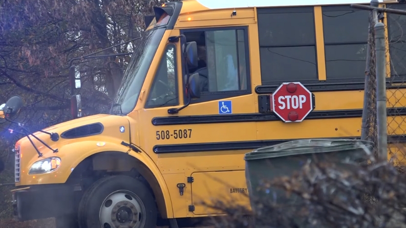 A Yellow School Bus with Its Stop Sign Extended, Parked Near a Fence